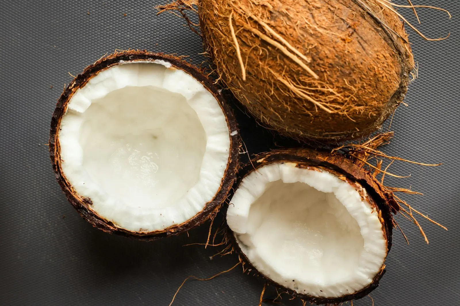 A whole husked coconut beside two halves showing the white kernel