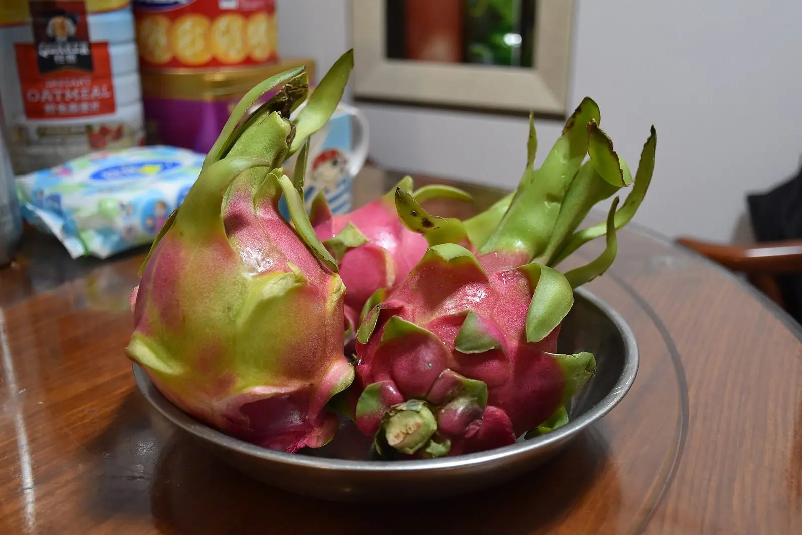 Whole dragon fruit with bright pink skin and green scales in a bowl