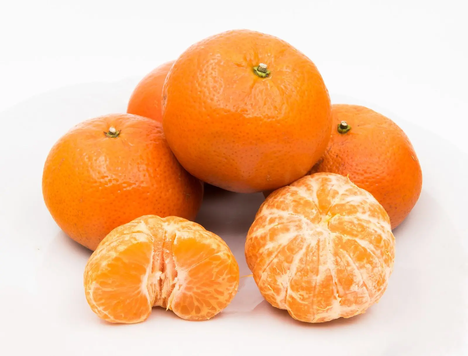 Whole mandarin oranges beside a peeled one broken into segments